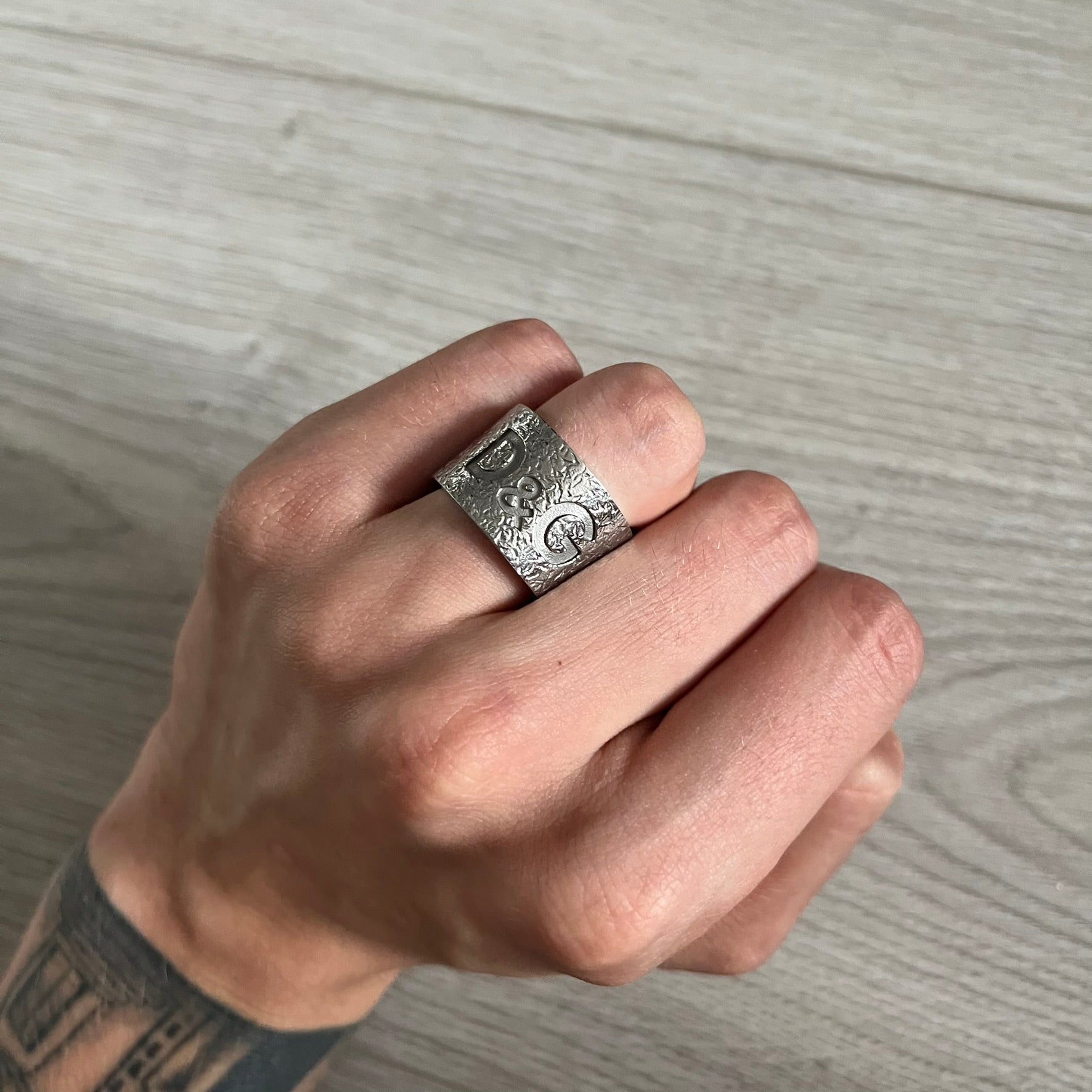 Hand wearing a silver ring with intricate design on a wooden surface