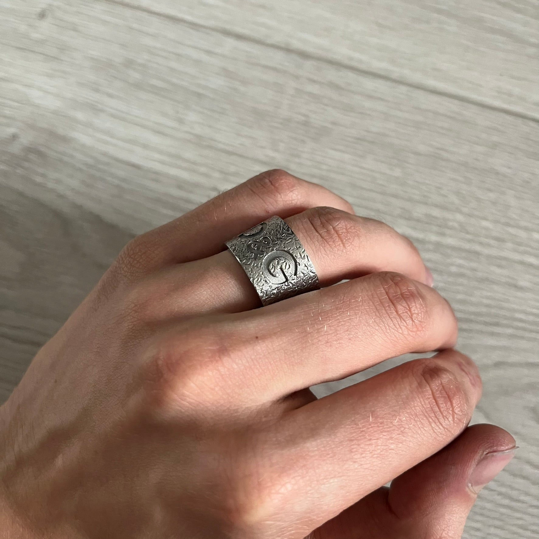 Silver ring with a design worn on a finger against a neutral background