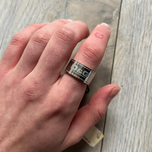 Dolce & Gabbana DJ0836 Logo Ring is a silver-tone stainless steel ring featuring engraved D&G logos in the center. The top and bottom edges have engraved rope-style lines running continuously around the band, giving it a subtle textured detail.