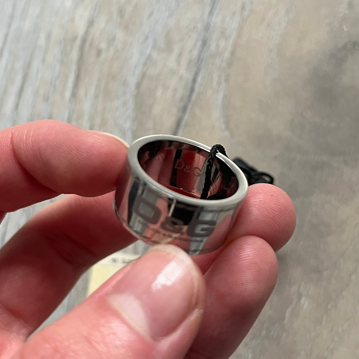 Dolce & Gabbana DJ0836 Logo Ring is a silver-tone stainless steel ring featuring engraved D&G logos in the center. The top and bottom edges have engraved rope-style lines running continuously around the band, giving it a subtle textured detail.