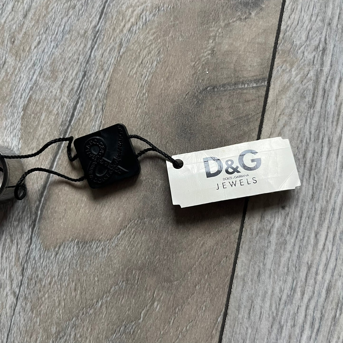 Dolce & Gabbana DJ0836 Logo Ring is a silver-tone stainless steel ring featuring engraved D&G logos in the center. The top and bottom edges have engraved rope-style lines running continuously around the band, giving it a subtle textured detail.