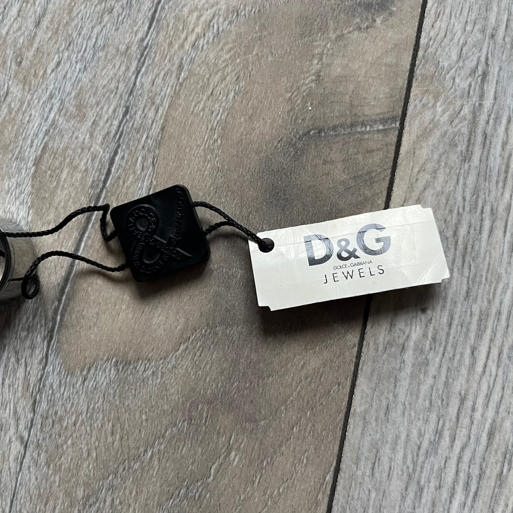 Dolce & Gabbana DJ0836 Logo Ring is a silver-tone stainless steel ring featuring engraved D&G logos in the center. The top and bottom edges have engraved rope-style lines running continuously around the band, giving it a subtle textured detail.