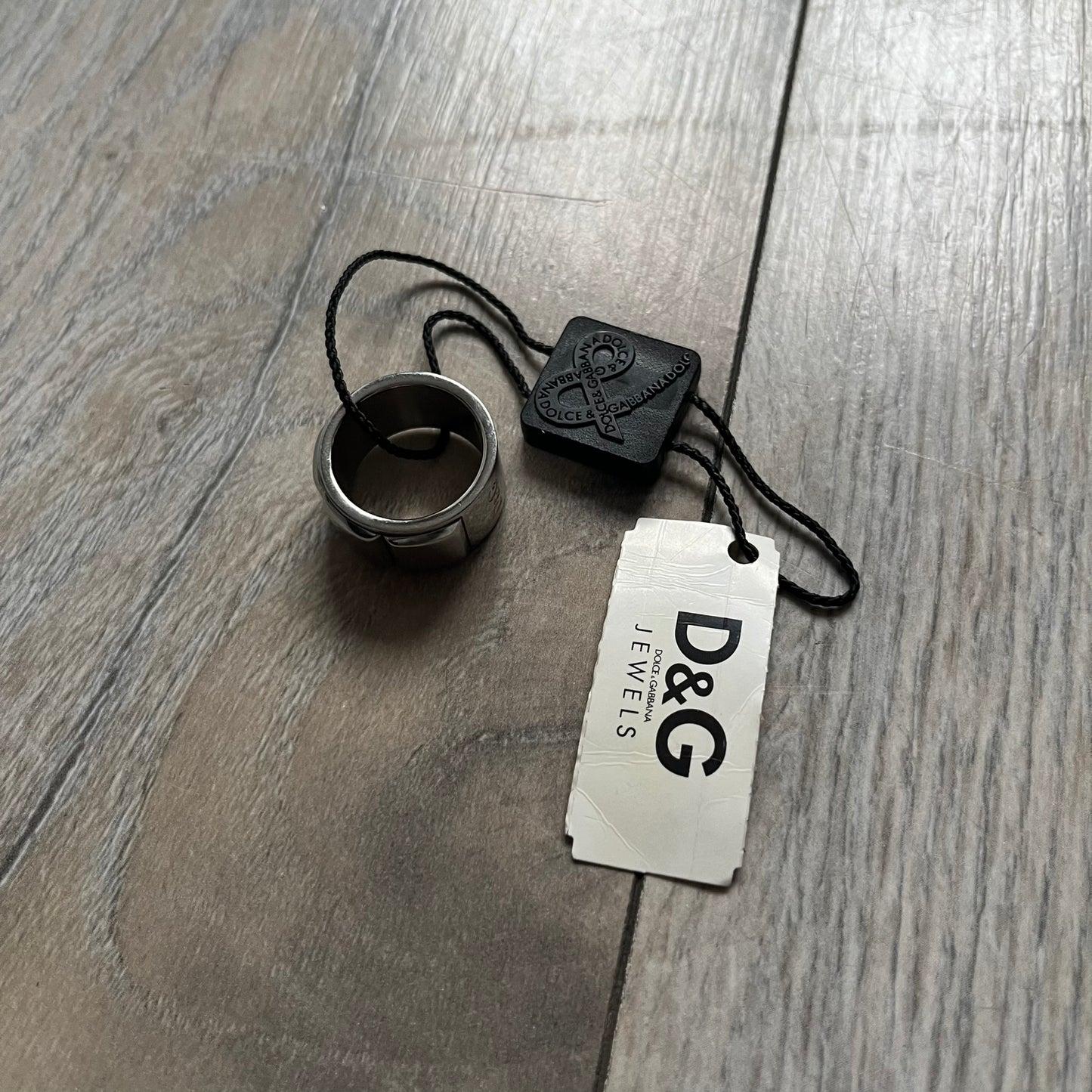 Dolce & Gabbana DJ0836 Ring is made from silver-tone metal and features three raised square elements set across the top. Next to the squares, there is a small engraved D&G logo. The ring has a clean, minimal design and is marked with model code DJ0836.