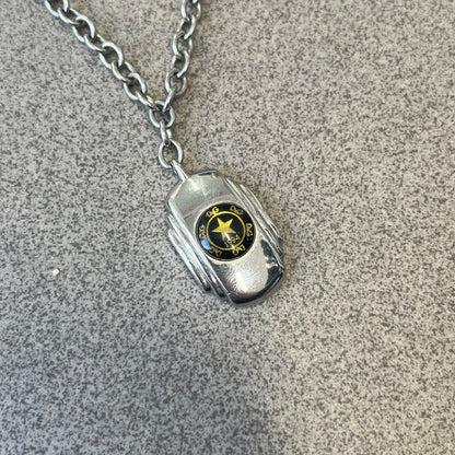 Dolce & Gabbana DJ1067 Gold Star Necklace features a silver-toned rectangular pendant with a black background and a circular plastic center, surrounded by gold D&G logos and a gold star with "1994" text. It comes on a circle-link chain with a large clasp.