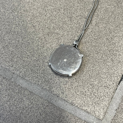 Dolce & Gabbana DJ1115 Circular Necklace is a stainless steel necklace with a circular pendant featuring a raised D&G logo in the center. A thin chain wraps around the pendant outline, held in place by small square clips at four points. It comes with a dust bag.