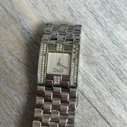 Dolce &amp; Gabbana Rhinestones Analog Watch is a stainless steel quartz watch featuring a square white dial with silver D&amp;G logo and silver hands. The case and bracelet form a continuous design with the face matching the width of the bracelet, and selected areas are set with crystal accents. It includes a dual side-clasp closure, is water resistant to 3 ATM, with removable links.