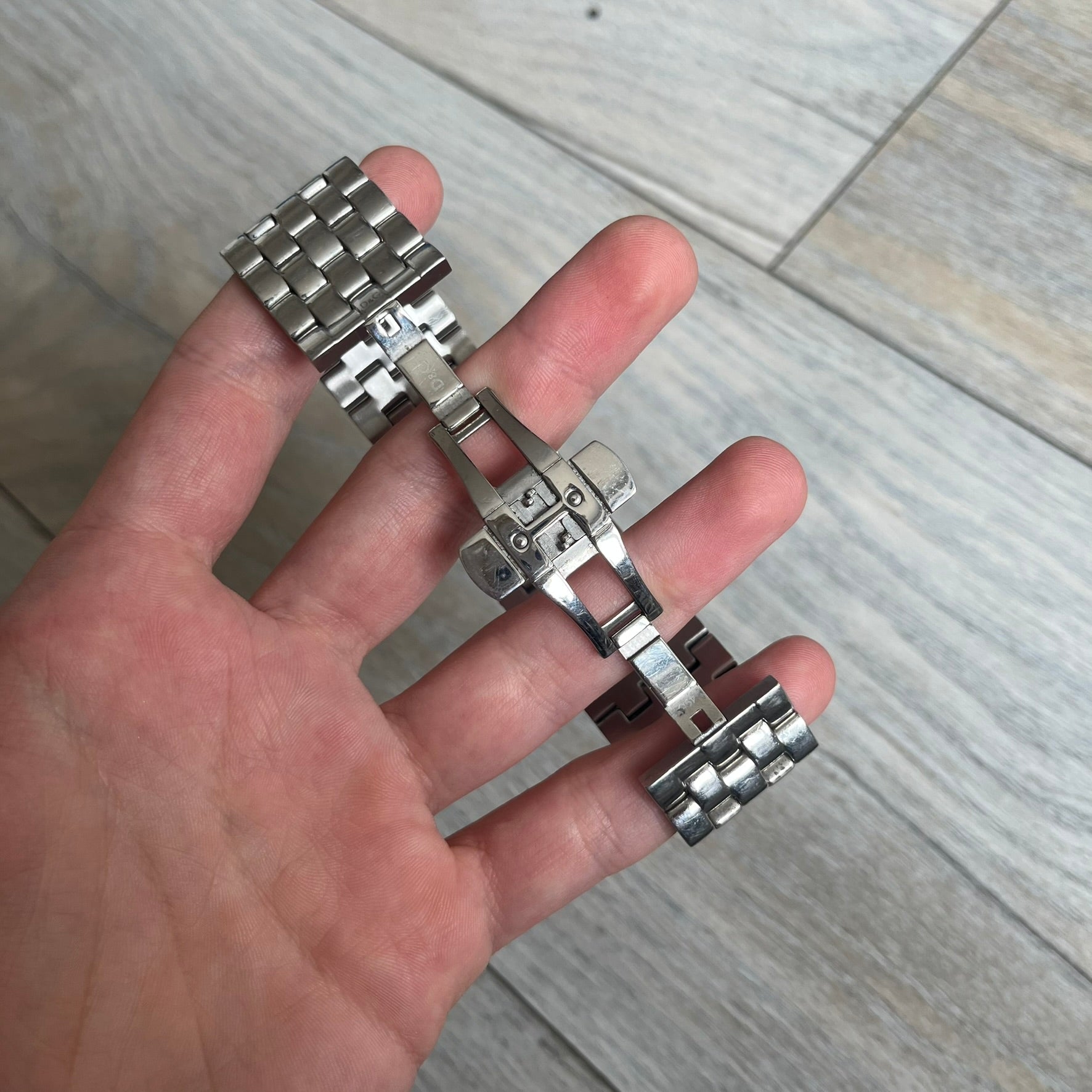 Dolce &amp; Gabbana Rhinestones Analog Watch is a stainless steel quartz watch featuring a square white dial with silver D&amp;G logo and silver hands. The case and bracelet form a continuous design with the face matching the width of the bracelet, and selected areas are set with crystal accents. It includes a dual side-clasp closure, is water resistant to 3 ATM, with removable links.