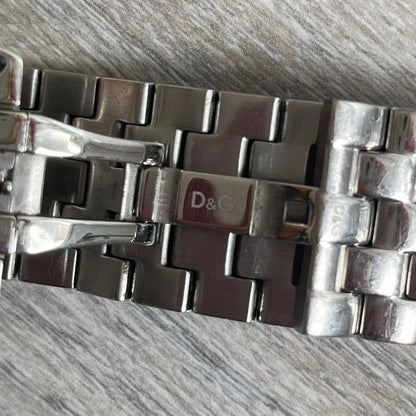 Dolce &amp; Gabbana Rhinestones Analog Watch is a stainless steel quartz watch featuring a square white dial with silver D&amp;G logo and silver hands. The case and bracelet form a continuous design with the face matching the width of the bracelet, and selected areas are set with crystal accents. It includes a dual side-clasp closure, is water resistant to 3 ATM, with removable links.