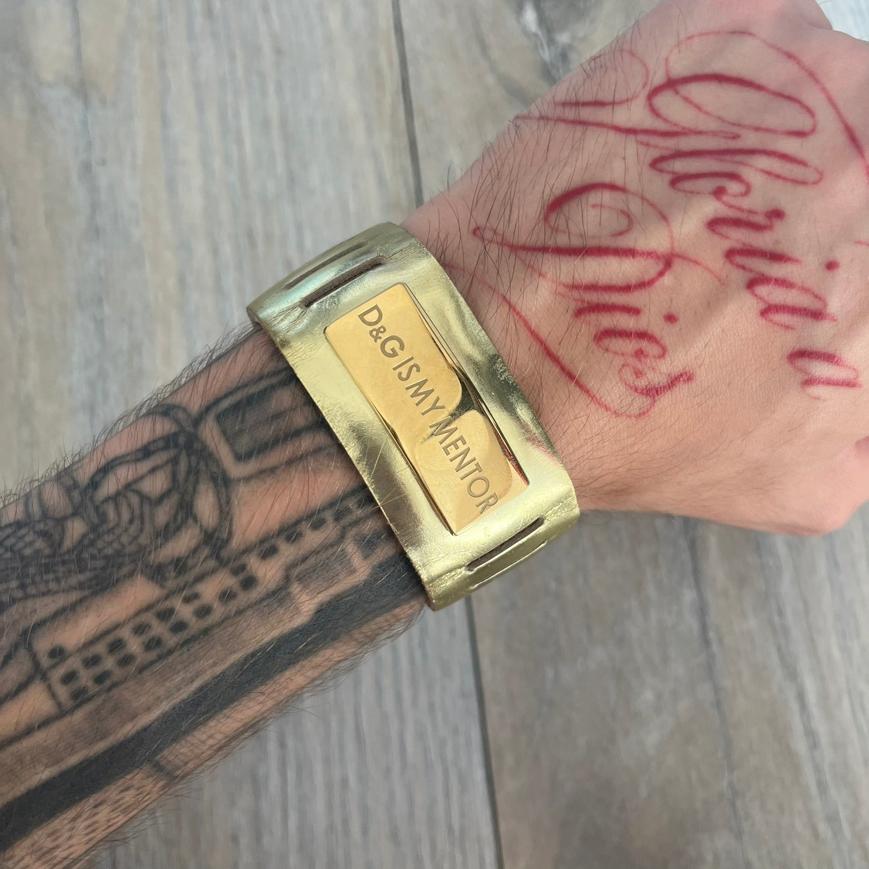 Dolce & Gabbana “D&G IS MY MENTOR” Bracelet is a gold leather bracelet with a glossy finish. The bracelet features line cutout detailing throughout and fastens with two snap-button closures on the back. A gold-tone metal plaque on the front is engraved with “D&G IS MY MENTOR.” The bracelet comes with its original box.
