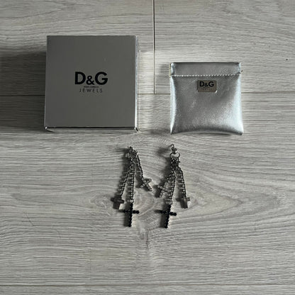 Dolce & Gabbana Dangle Drop Cross Earrings. Pair of earrings featuring three crosses of varying lengths on each, including one with black stones, one with clear stones, and one full metal cross with a D&G logo and a small clear stone. Comes with original box and dustbag