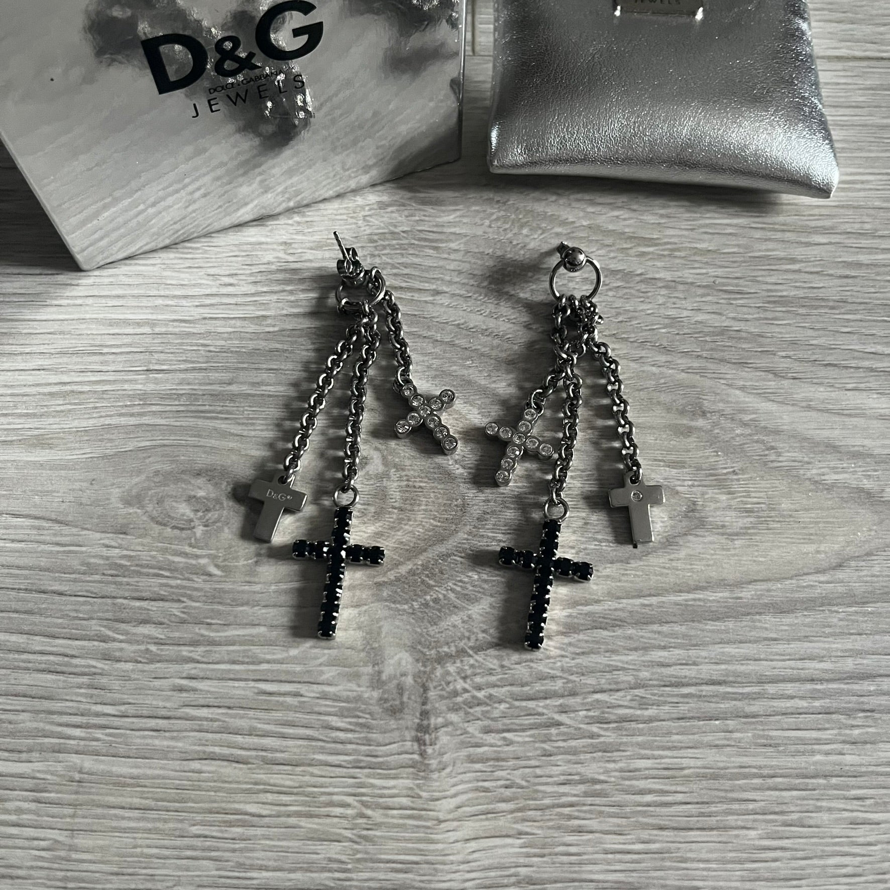 Dolce & Gabbana Dangle Drop Cross Earrings. Pair of earrings featuring three crosses of varying lengths on each, including one with black stones, one with clear stones, and one full metal cross with a D&G logo and a small clear stone. Comes with original box and dustbag