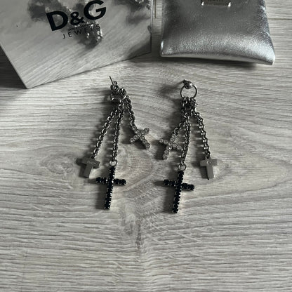 Dolce & Gabbana Dangle Drop Cross Earrings. Pair of earrings featuring three crosses of varying lengths on each, including one with black stones, one with clear stones, and one full metal cross with a D&G logo and a small clear stone. Comes with original box and dustbag