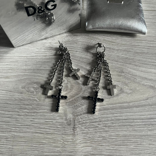 Dolce & Gabbana Dangle Drop Cross Earrings. Pair of earrings featuring three crosses of varying lengths on each, including one with black stones, one with clear stones, and one full metal cross with a D&G logo and a small clear stone. Comes with original box and dustbag