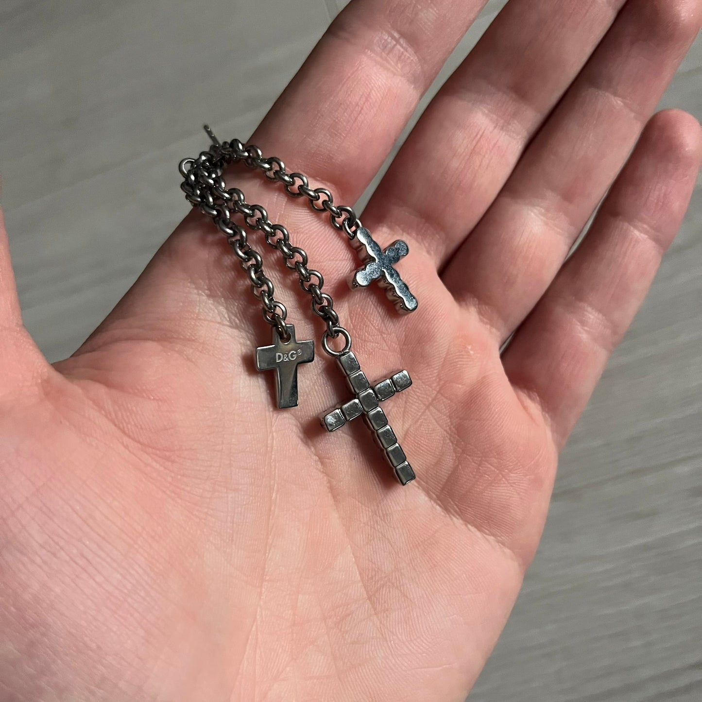 Dolce & Gabbana Dangle Drop Cross Earrings. Pair of earrings featuring three crosses of varying lengths on each, including one with black stones, one with clear stones, and one full metal cross with a D&G logo and a small clear stone. Comes with original box and dustbag