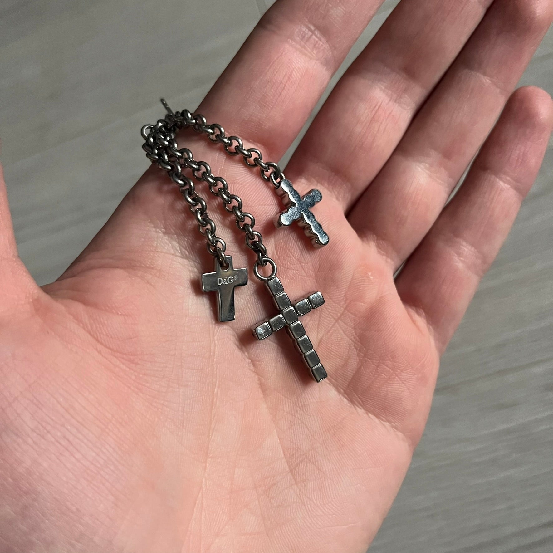 Dolce & Gabbana Dangle Drop Cross Earrings. Pair of earrings featuring three crosses of varying lengths on each, including one with black stones, one with clear stones, and one full metal cross with a D&G logo and a small clear stone. Comes with original box and dustbag