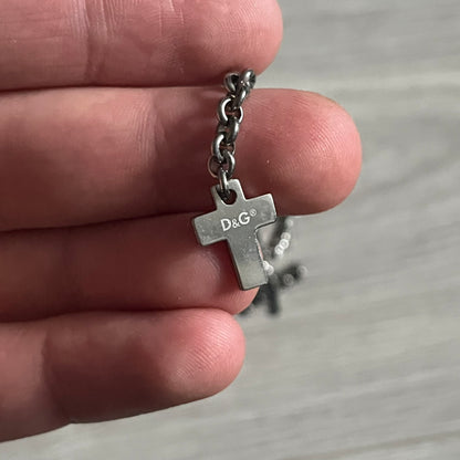 Dolce & Gabbana Dangle Drop Cross Earrings. Pair of earrings featuring three crosses of varying lengths on each, including one with black stones, one with clear stones, and one full metal cross with a D&G logo and a small clear stone. Comes with original box and dustbag