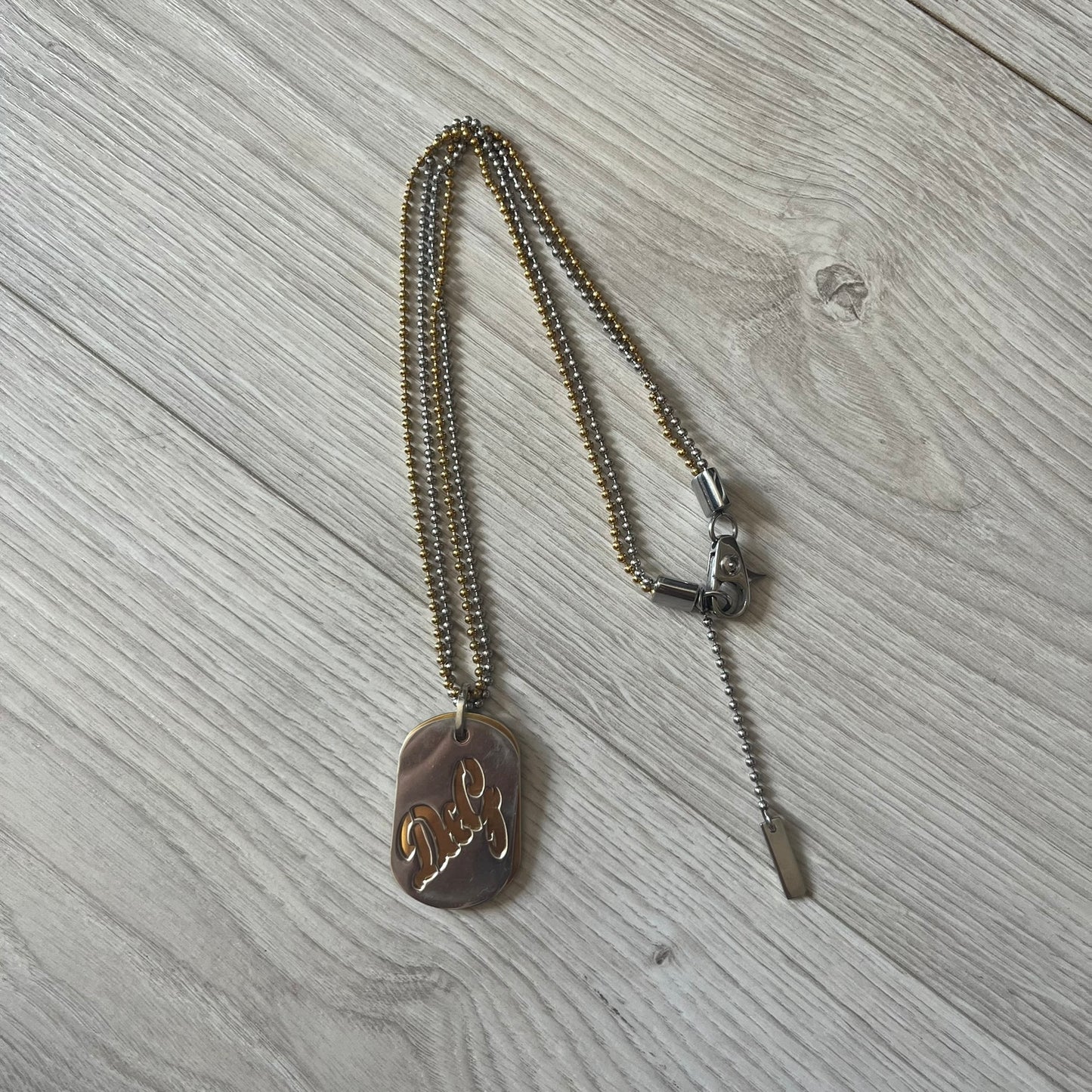 Dolce & Gabbana double dog tag necklace featuring two layered pendants: a clear gold-tone tag underneath and a silver-tone tag on top with a cut-out D&amp;G logo revealing the gold beneath. Designed with both silver and gold chains, it creates a striking two-tone effect.