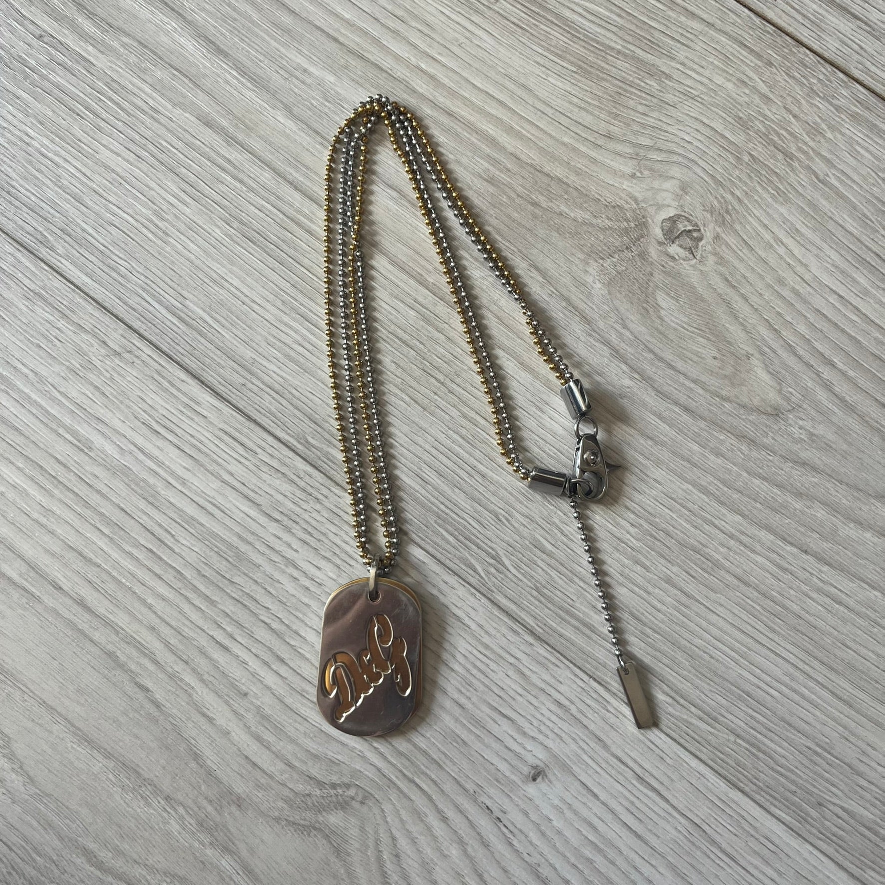 Dolce & Gabbana double dog tag necklace featuring two layered pendants: a clear gold-tone tag underneath and a silver-tone tag on top with a cut-out D&amp;G logo revealing the gold beneath. Designed with both silver and gold chains, it creates a striking two-tone effect.