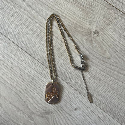 Dolce & Gabbana double dog tag necklace featuring two layered pendants: a clear gold-tone tag underneath and a silver-tone tag on top with a cut-out D&amp;G logo revealing the gold beneath. Designed with both silver and gold chains, it creates a striking two-tone effect.