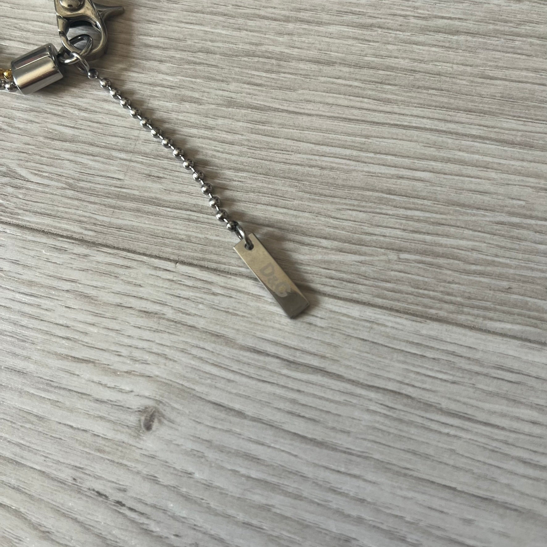 Dolce & Gabbana double dog tag necklace featuring two layered pendants: a clear gold-tone tag underneath and a silver-tone tag on top with a cut-out D&amp;G logo revealing the gold beneath. Designed with both silver and gold chains, it creates a striking two-tone effect.