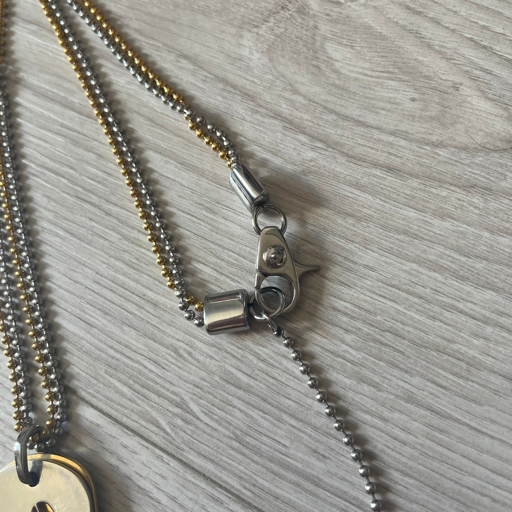 Dolce & Gabbana double dog tag necklace featuring two layered pendants: a clear gold-tone tag underneath and a silver-tone tag on top with a cut-out D&amp;G logo revealing the gold beneath. Designed with both silver and gold chains, it creates a striking two-tone effect.