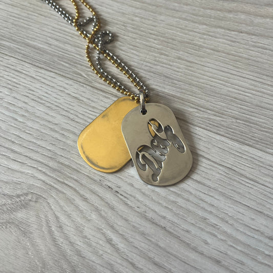 Dolce &amp; Gabbana double dog tag necklace featuring two layered pendants: a clear gold-tone tag underneath and a silver-tone tag on top with a cut-out D&amp;G logo revealing the gold beneath. Designed with both silver and gold chains, it creates a striking two-tone effect.