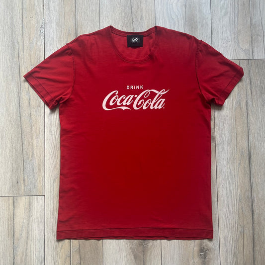 Dolce &amp; Gabbana Fall 2011 tee in vibrant red featuring a simple “Drink Coca-Cola” logo on the chest. Designed with an inside-out stitching aesthetic and a subtle back logo under the collar. A unique, collectible tee that merges casual branding with high-fashion flair.