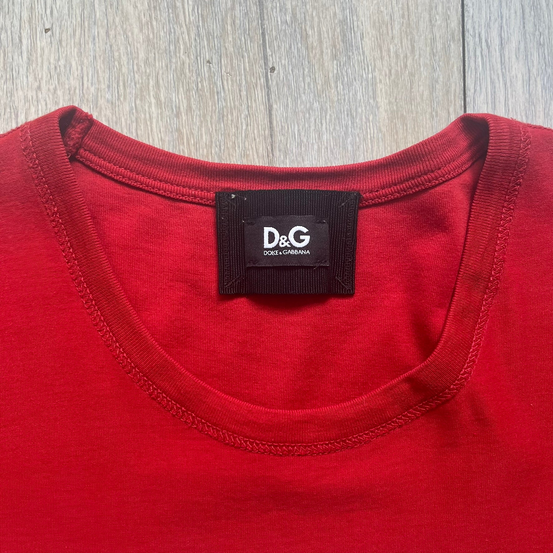 Dolce &amp; Gabbana Fall 2011 tee in vibrant red featuring a simple “Drink Coca-Cola” logo on the chest. Designed with an inside-out stitching aesthetic and a subtle back logo under the collar. A unique, collectible tee that merges casual branding with high-fashion flair.