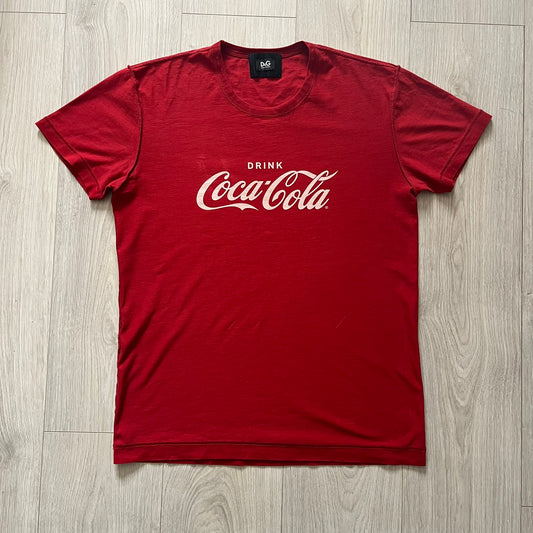 Dolce &amp; Gabbana Fall 2011 tee in vibrant red featuring a simple “Drink Coca-Cola” logo on the chest. Designed with an inside-out stitching aesthetic and a subtle back logo under the collar. A unique, collectible tee that merges casual branding with high-fashion flair.