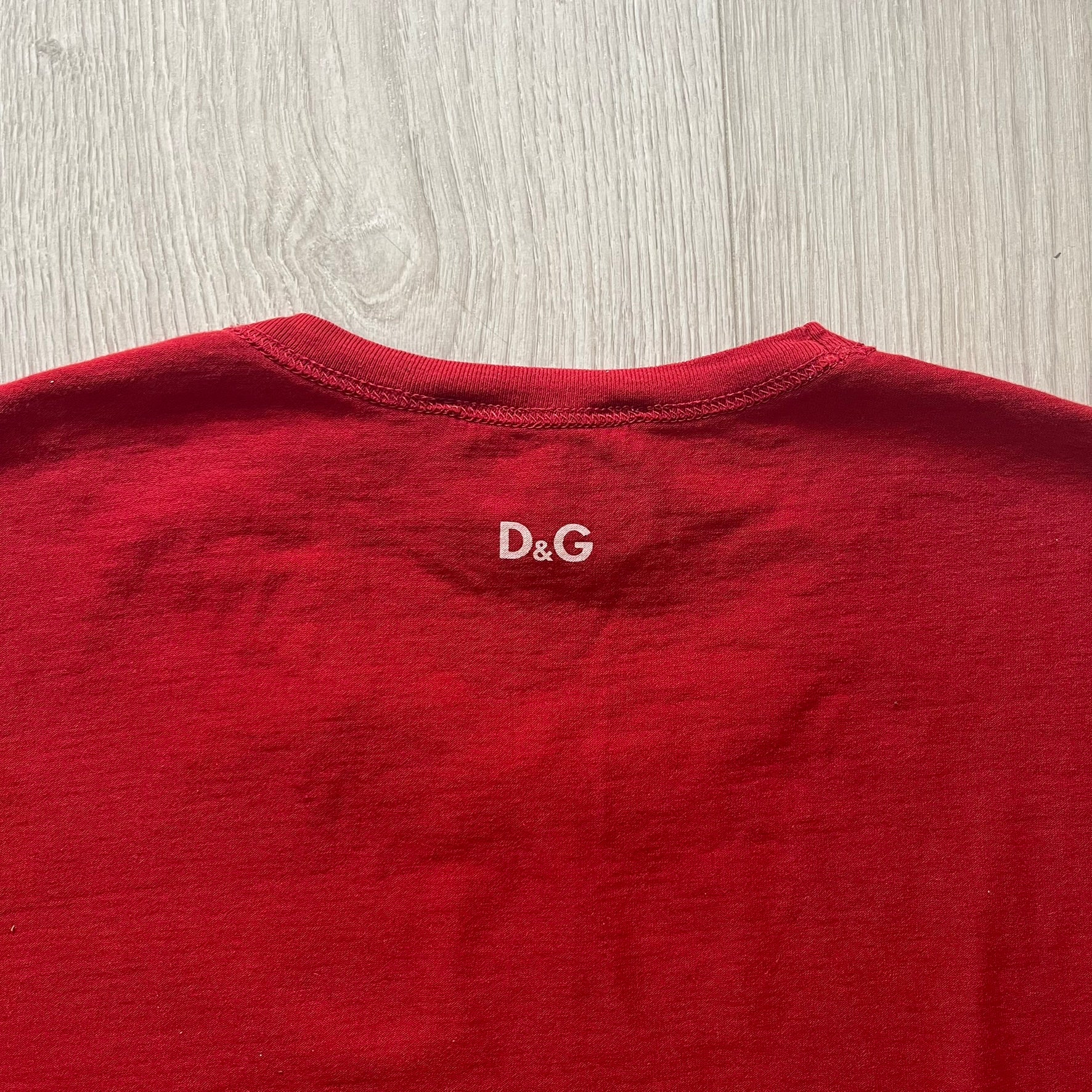 Dolce &amp; Gabbana Fall 2011 tee in vibrant red featuring a simple “Drink Coca-Cola” logo on the chest. Designed with an inside-out stitching aesthetic and a subtle back logo under the collar. A unique, collectible tee that merges casual branding with high-fashion flair.