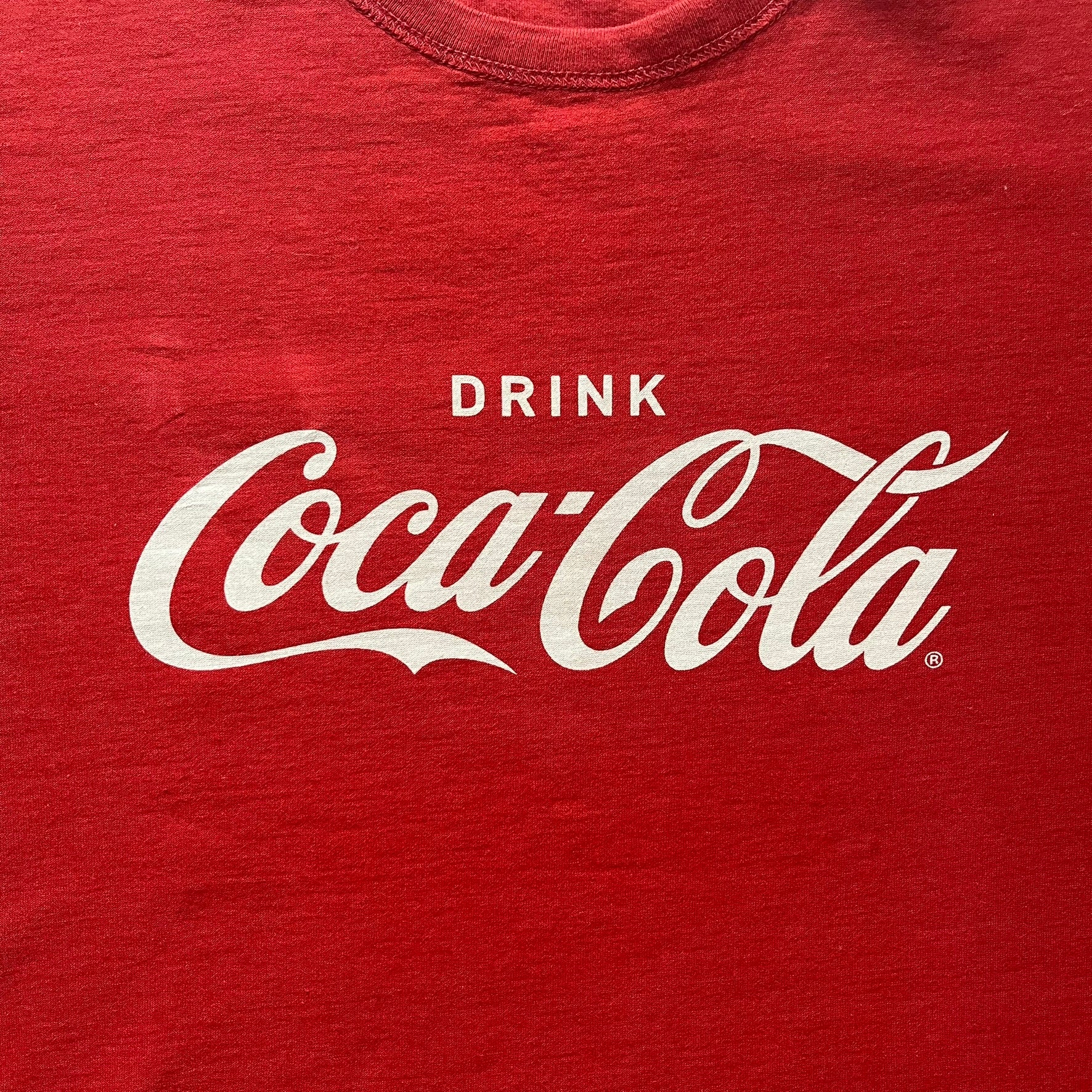 Dolce &amp; Gabbana Fall 2011 tee in vibrant red featuring a simple “Drink Coca-Cola” logo on the chest. Designed with an inside-out stitching aesthetic and a subtle back logo under the collar. A unique, collectible tee that merges casual branding with high-fashion flair.