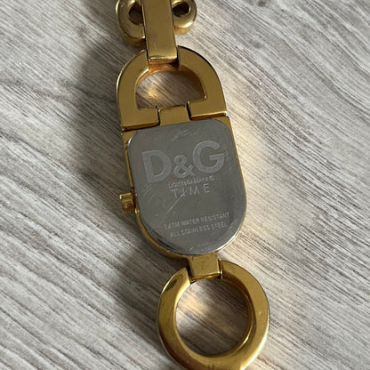 Gold and silver keychain with D&G logo on a gray surface