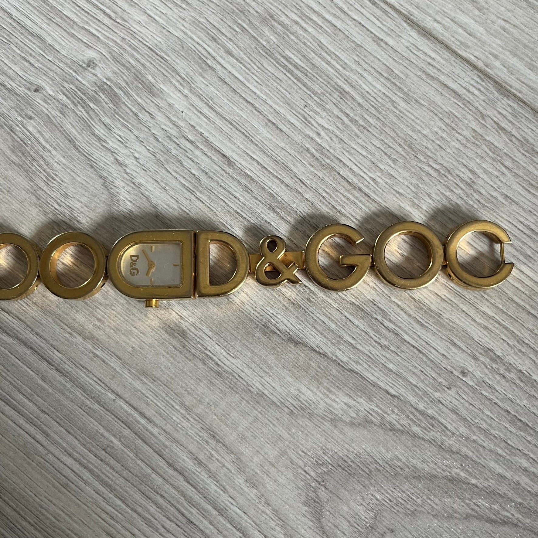 Gold bracelet with 'D&G' logo on a gray wooden surface