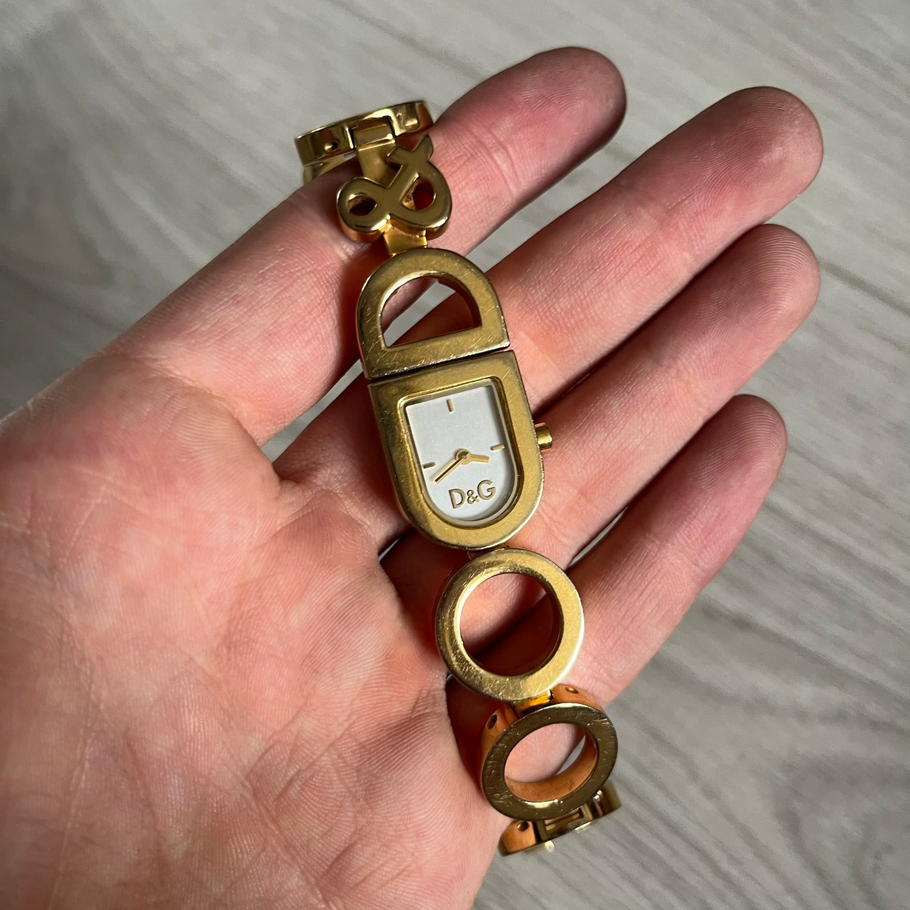 Gold watch with a white face held in a hand against a neutral background