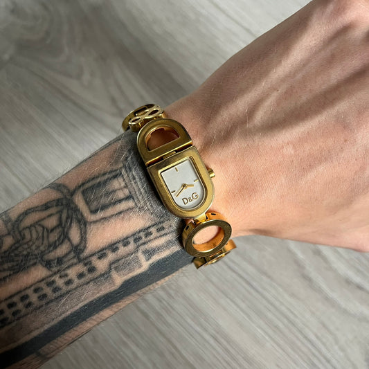 Gold wristwatch with a visible brand logo on a wrist with tattoos.