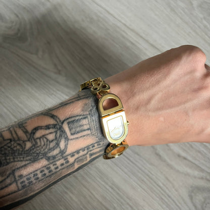 Gold watch on a wrist with tattoos against a gray background