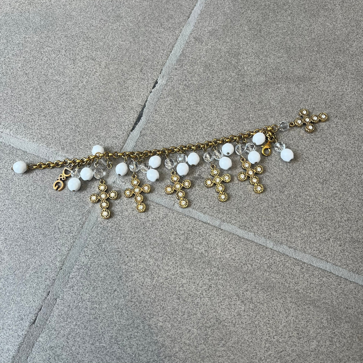 Dolce &amp; Gabbana Gold Charm Cross DJ0250 Bracelet features a gold-tone chain bracelet with white bead charms, six cross-shaped charms made from circular elements, and a D&amp;G logo charm. The bracelet has a gold-tone metal construction.&nbsp;