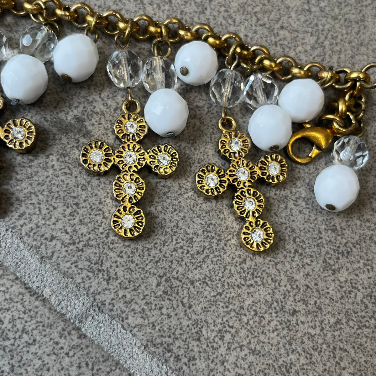 Dolce &amp; Gabbana Gold Charm Cross DJ0250 Bracelet features a gold-tone chain bracelet with white bead charms, six cross-shaped charms made from circular elements, and a D&amp;G logo charm. The bracelet has a gold-tone metal construction.&nbsp;