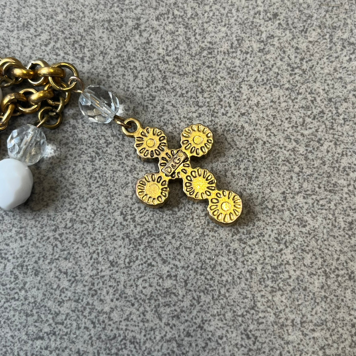 Dolce &amp; Gabbana Gold Charm Cross DJ0250 Bracelet features a gold-tone chain bracelet with white bead charms, six cross-shaped charms made from circular elements, and a D&amp;G logo charm. The bracelet has a gold-tone metal construction.&nbsp;