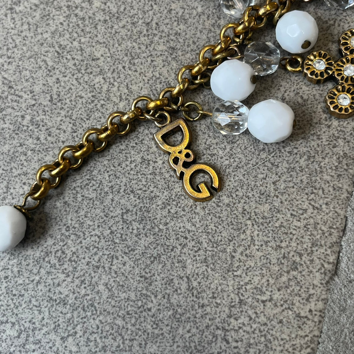 Dolce &amp; Gabbana Gold Charm Cross DJ0250 Bracelet features a gold-tone chain bracelet with white bead charms, six cross-shaped charms made from circular elements, and a D&amp;G logo charm. The bracelet has a gold-tone metal construction.&nbsp;