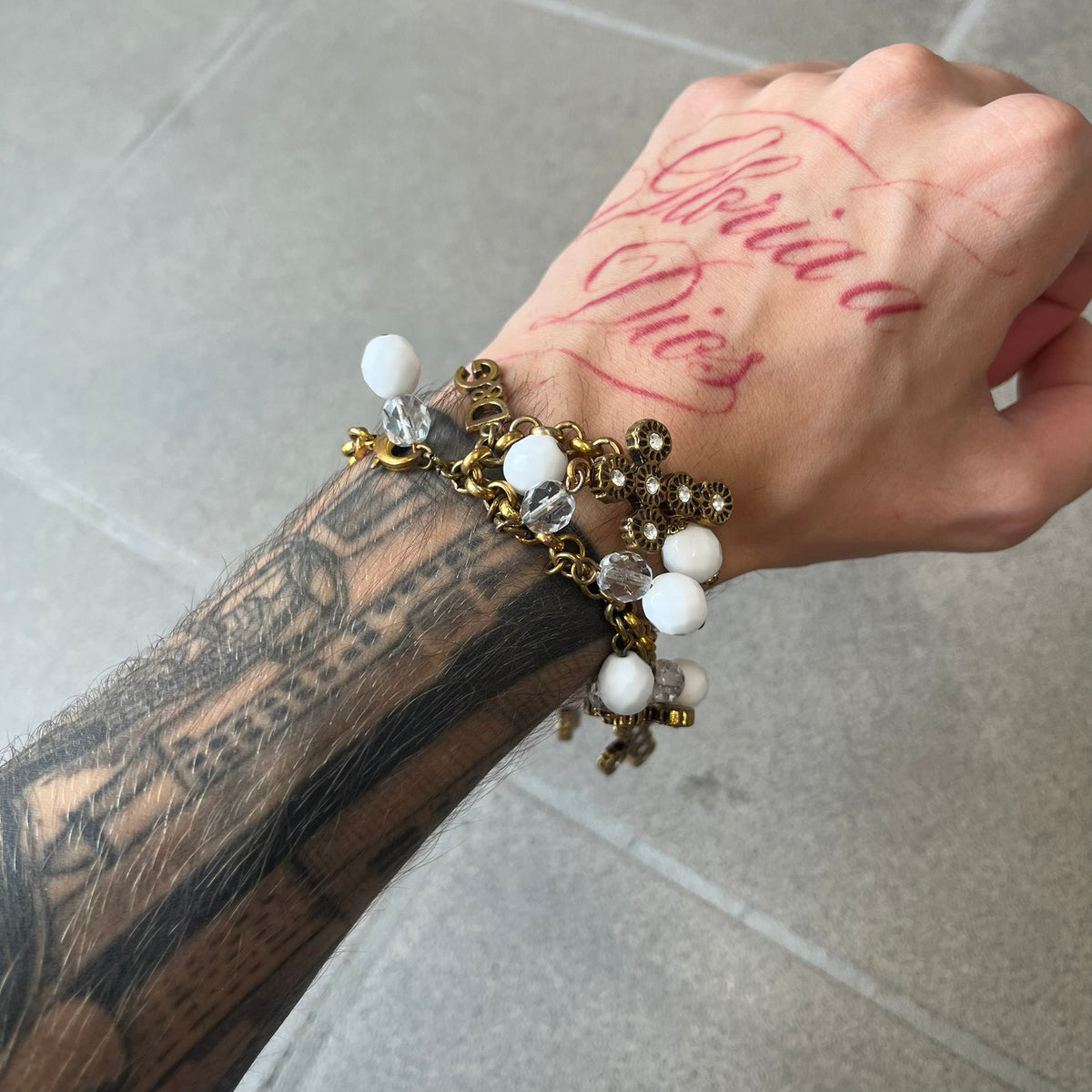Dolce &amp; Gabbana Gold Charm Cross DJ0250 Bracelet features a gold-tone chain bracelet with white bead charms, six cross-shaped charms made from circular elements, and a D&amp;G logo charm. The bracelet has a gold-tone metal construction.&nbsp;