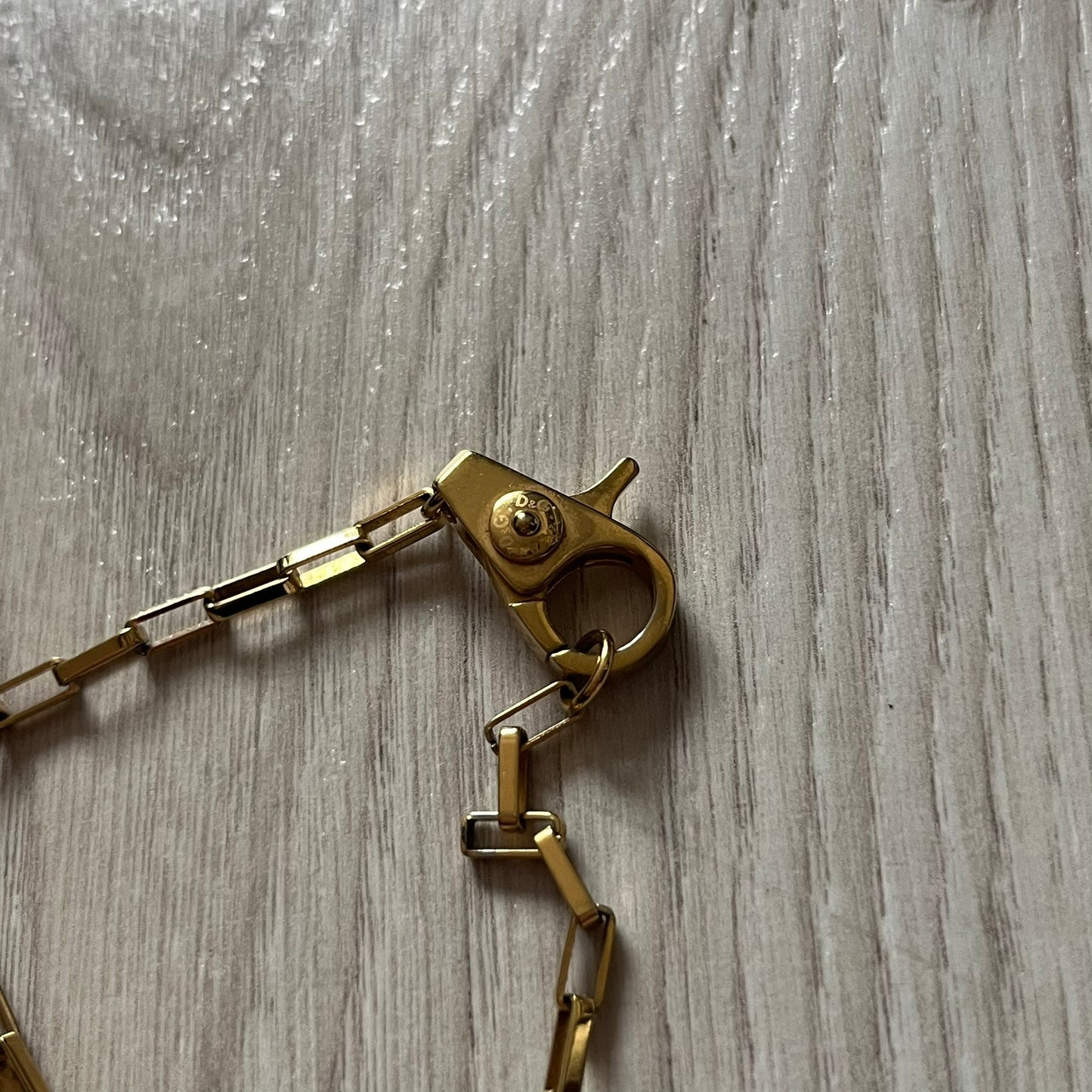 The Dolce & Gabbana Teddy Bear Necklace from the 2000s features a flat gold-tone teddy bear pendant detailed with six visible screws and a small D&G logo at the bottom. It hangs from a paperclip chain with a lobster clasp closure, it comes with a silver D&G Jewels bag.