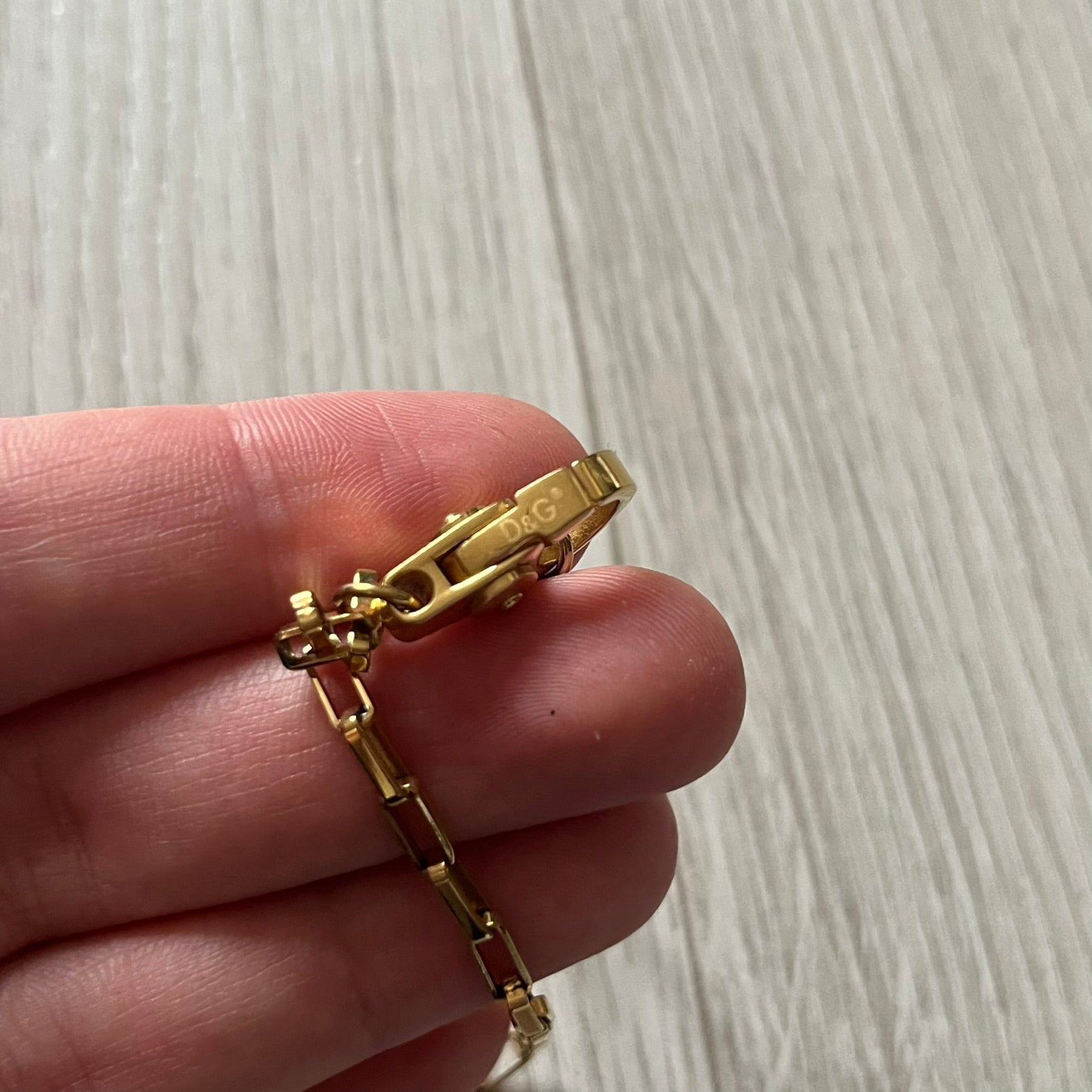 The Dolce & Gabbana Teddy Bear Necklace from the 2000s features a flat gold-tone teddy bear pendant detailed with six visible screws and a small D&G logo at the bottom. It hangs from a paperclip chain with a lobster clasp closure, it comes with a silver D&G Jewels bag.