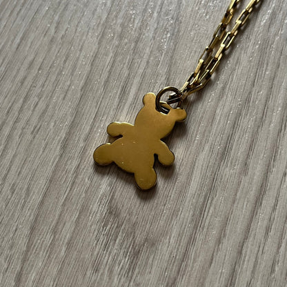 The Dolce & Gabbana Teddy Bear Necklace from the 2000s features a flat gold-tone teddy bear pendant detailed with six visible screws and a small D&G logo at the bottom. It hangs from a paperclip chain with a lobster clasp closure, it comes with a silver D&G Jewels bag.