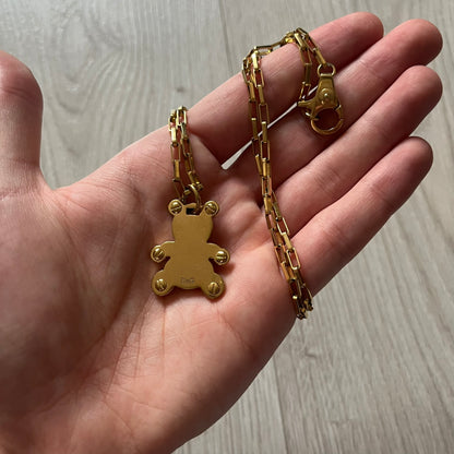 The Dolce & Gabbana Teddy Bear Necklace from the 2000s features a flat gold-tone teddy bear pendant detailed with six visible screws and a small D&G logo at the bottom. It hangs from a paperclip chain with a lobster clasp closure, it comes with a silver D&G Jewels bag.