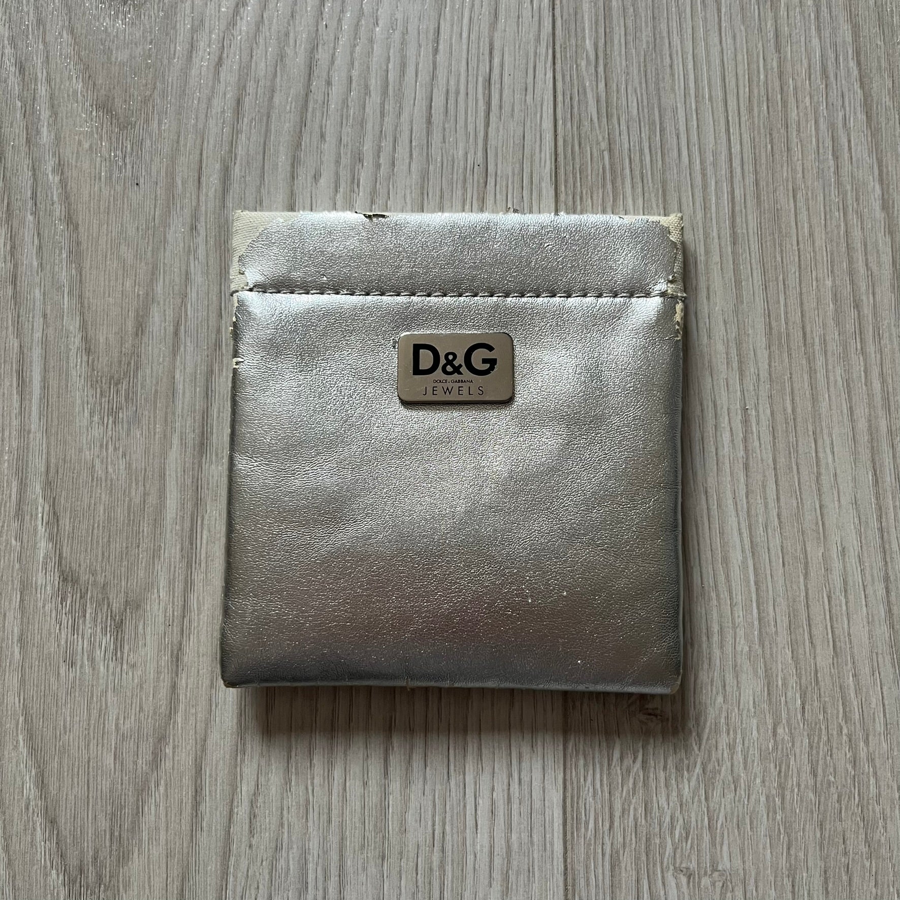 The Dolce & Gabbana Teddy Bear Necklace from the 2000s features a flat gold-tone teddy bear pendant detailed with six visible screws and a small D&G logo at the bottom. It hangs from a paperclip chain with a lobster clasp closure, it comes with a silver D&G Jewels bag.