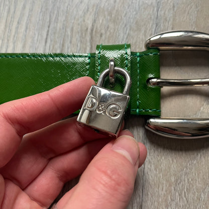 Dolce & Gabbana Green Leather Padlock Buckle Belt features a shiny green leather strap with a beige leather underside. The belt has metal-outlined eyelets for the holes and a clean, simple silver-tone buckle. Next to the buckle is a silver-tone padlock engraved with D&G, along with a fixed metal loop at the center of the belt intended to attach a chain (chain not included).
