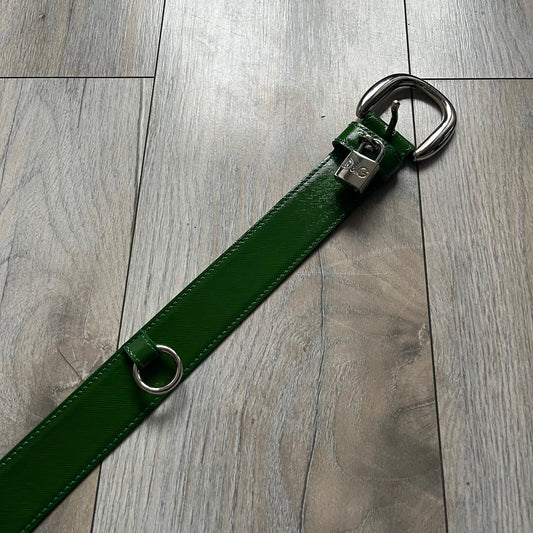 Dolce & Gabbana Green Leather Padlock Buckle Belt features a shiny green leather strap with a beige leather underside. The belt has metal-outlined eyelets for the holes and a clean, simple silver-tone buckle. Next to the buckle is a silver-tone padlock engraved with D&G, along with a fixed metal loop at the center of the belt intended to attach a chain (chain not included).