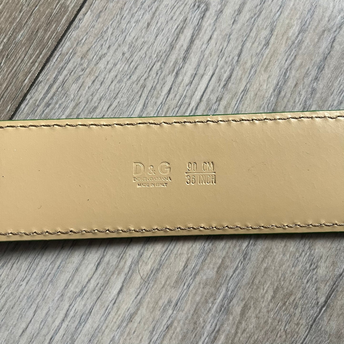 Dolce & Gabbana Green Leather Padlock Buckle Belt features a shiny green leather strap with a beige leather underside. The belt has metal-outlined eyelets for the holes and a clean, simple silver-tone buckle. Next to the buckle is a silver-tone padlock engraved with D&G, along with a fixed metal loop at the center of the belt intended to attach a chain (chain not included).