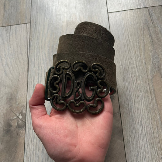 Dolce & Gabbana Green Suede Hearts Belt is made from very dark green suede with an orange leather interior featuring large dot detailing. The buckle is a metal D&G logo surrounded by eight heart shapes pointing outward, all finished in a dark, aged-looking metal tone. The belt comes with the original hologram tag attached.